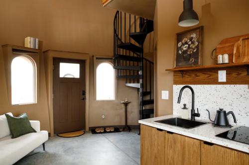 Cozy interior of a small home featuring a spiral staircase, kitchen area, and a door with arched windows.